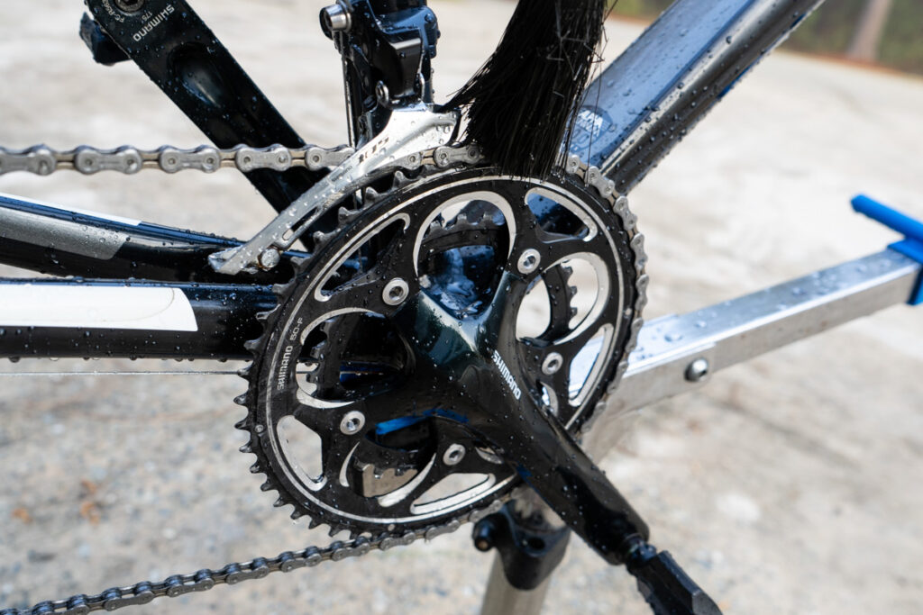 A brush is applying degreaser to clean the bike chain and drivetrain.